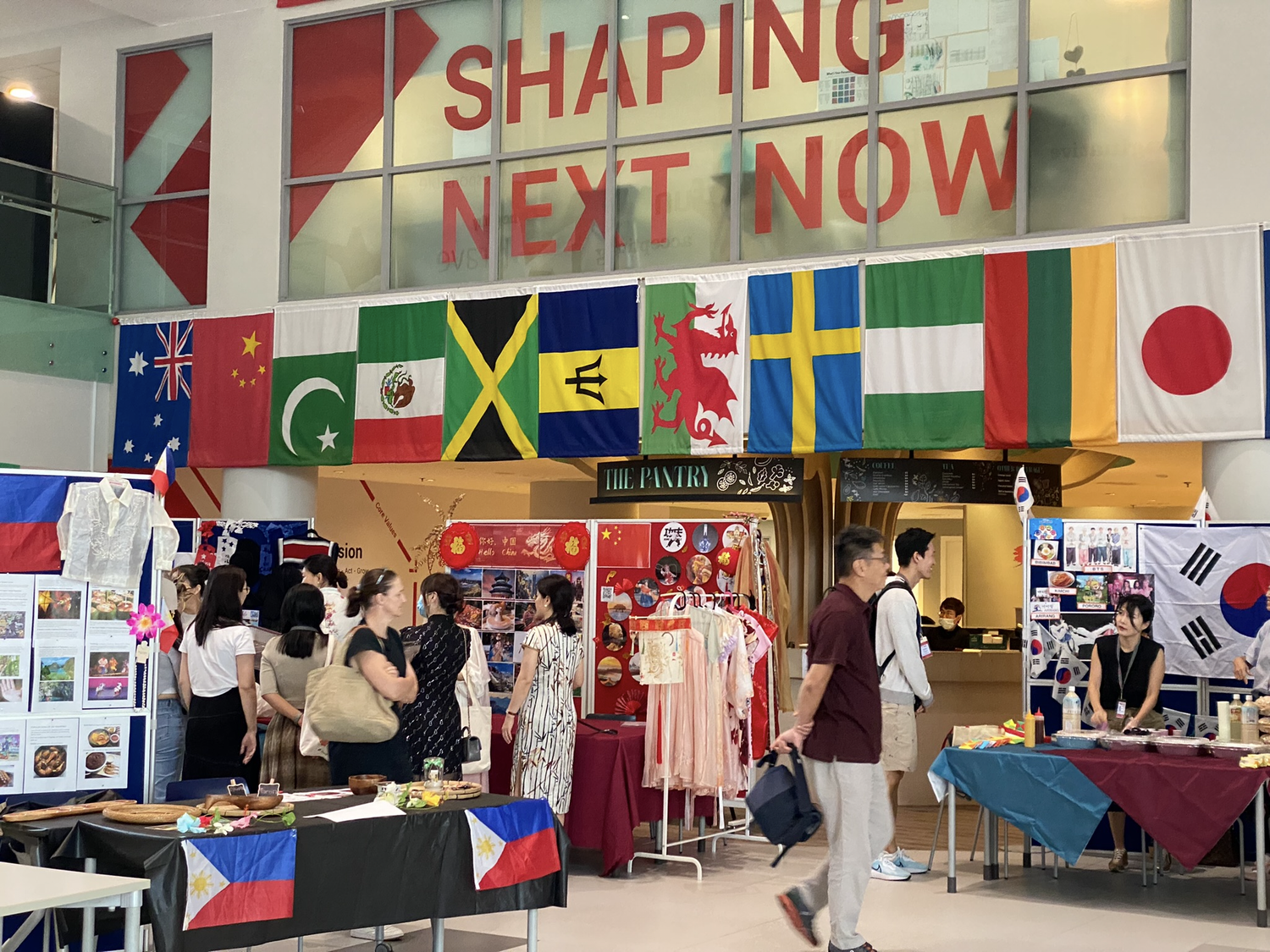 「SHAPING NEXT NOW」の文字と各国の国旗が掲げられた会場に並ぶ展示ブース